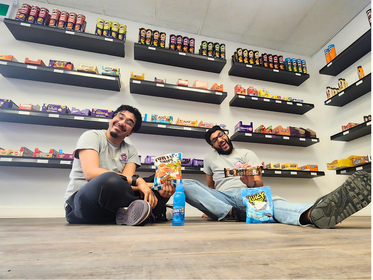 Two Owners sitting on the floor of a exotic store with snacks and drinks.